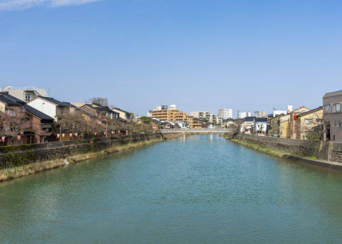 A river lined with houses in Kanazawa, shot on a day with clear, blue skies.